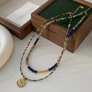 Detail of double-layered beaded necklace with gold coin pendant on vintage jewelry box