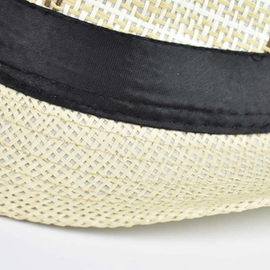 Macro detail of beige woven fedora hat featuring a black satin band and fine stitching