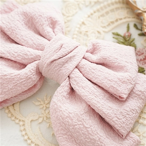 Detailed close-up of a pink textured fabric bow hairclip showing fine material weave