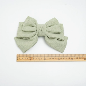 Pale green triple layer bow hair clip in textured fabric with ruler for scale