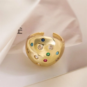 Detail of a gold wide-band ring with colorful zircons on soft beige silk fabric