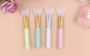 Flat lay of four silicone face mask brushes with plastic handles on beige felt background