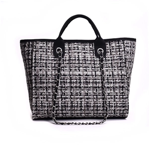 Close-up of black and white checkered tweed texture with silver chain strap on tote bag