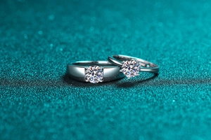 Macro shot of silver Moissanite couple rings with round cut diamond on teal glitter background