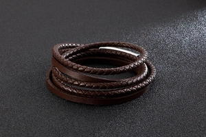 Close-up of brown multilayer braided leather bracelet with silver metal clasp on black surface