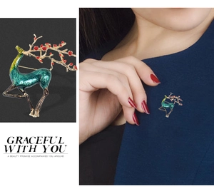 Detail of green enamel elk brooch with golden antlers shown on a model and close-up