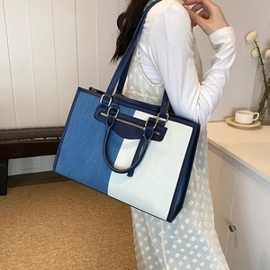 Close-up of contrast canvas tote bag featuring denim patchwork and leather handle details