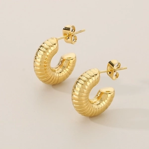 Macro detail of gold-plated croissant hoop earrings with elegant ribbed texture