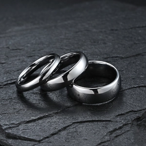 Three polished silver tungsten rings of varying widths on a dark textured rock surface