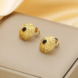 Close-up of gold earrings with black oval gemstone and vintage hollow pattern