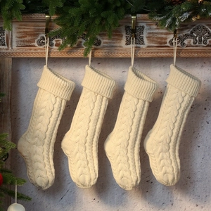 Set of four cream cable knit Christmas stockings hanging on a festive wooden mantel