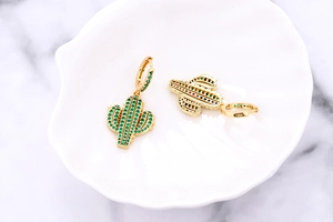 Detail of golden cactus earrings with green zircon pave setting on a marble surface