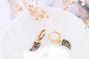 Close-up of gold horn earrings with colorful zircon stones on white ceramic dish