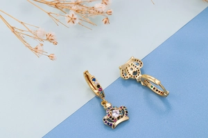 Detailed macro view of a gold crown earring with colorful zircon stones on blue background