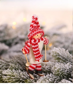 Close-up of a wooden skiing doll ornament with red knit hat on snowy pine branches