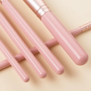 Close-up of five pink makeup brushes with rose gold ferrules on a soft beige background