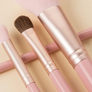 Detailed close-up of pink and rose gold makeup brushes with soft bristles on beige surface