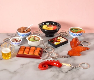 Detailed close-up of realistic PVC food keychains like ramen and beer on marble table