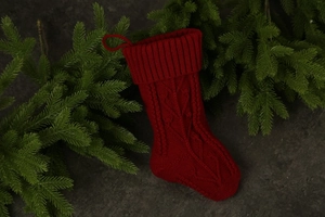 Close-up of a red cable-knit Christmas stocking with a hanging loop on pine branches