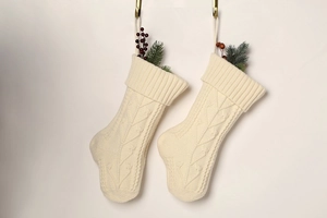 Detail of two cream knitted Christmas stockings with cable patterns and berry sprigs