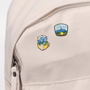 Outdoor wilderness enamel pins with mountain and forest themes on a cream canvas backpack