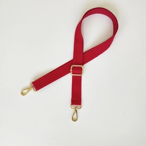Détail de la bandoulière en toile rouge avec boucle et crochets en métal doré réglables