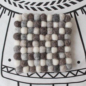 Close-up of square wool felt ball coaster in checkered grey and brown pattern