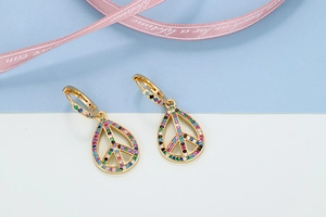 Detailed close-up of gold peace sign earrings with multi-color cubic zirconia stones