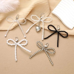 Close-up of beaded bowtie keychains with pearls and metallic charms on soft fabric