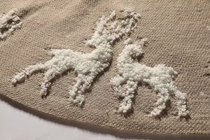 Close-up of beige knitted Christmas tree skirt featuring a white plush reindeer detail