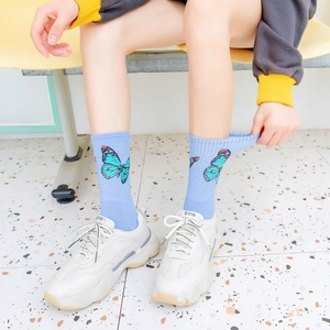 Detail of light blue crew socks with butterfly pattern shown on a model with white shoes