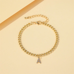 Bracelet de cheville doré avec pendentif initiale A strassé sur fond beige épuré