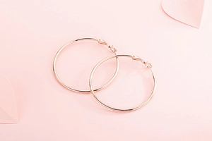 Gros plan de créoles en acier inoxydable or rose sur fond rose romantique