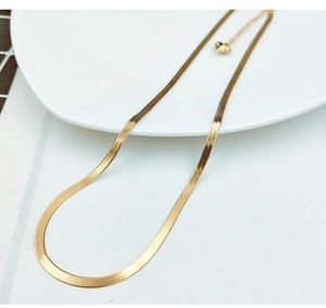 Detail of golden snake chain necklace with heart pendant on a white ceramic plate
