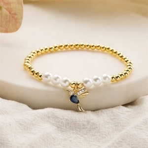 Macro shot of gold beads and white pearls bracelet featuring a blue hummingbird charm