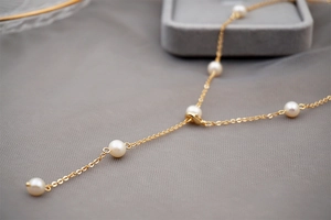 Detail of adjustable gold Y-shaped necklace with small freshwater pearls on fabric
