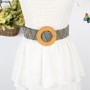 Detail of woven straw belt with black and white pattern and round buckle on white dress