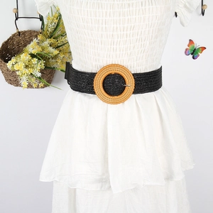Detail of a black woven straw belt featuring a round natural rattan buckle for dresses
