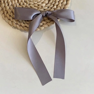 Detail of grey-purple satin ribbon bow hair clip with long streamers on woven mat