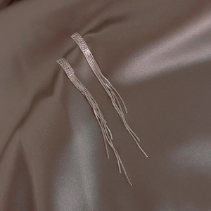 Orecchini pendenti lunghi in argento con nappe e cristalli geometrici su sfondo di seta