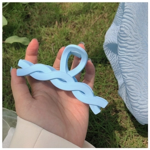 Close-up of light blue twisted matte hair claw clip held against a soft fabric background