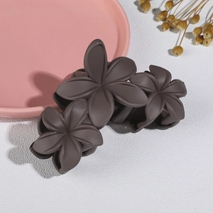 Detailed macro view of matte coffee brown flower hair claw clip on a textured table
