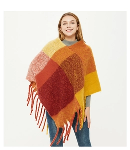 Close-up of thick knitted plaid poncho with fringe details in orange, red and yellow hues