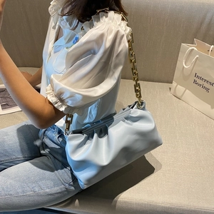 Detail of light blue pleated cloud bag featuring chunky gold chain strap and soft texture