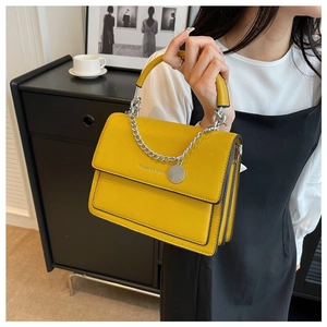 Detail of yellow leather handbag showing silver chain decor and textured flap surface