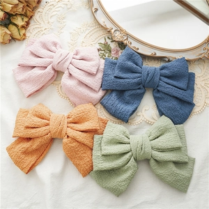 Flat lay of four colorful textured fabric bow hair clips in pink, blue, orange and green