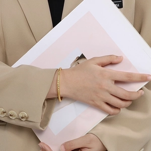 Detail of a gold-plated faceted bangle on wrist, styled with a warm-toned professional blazer