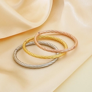 Detail of twisted metal bangles in gold, silver, and rose gold on silk fabric