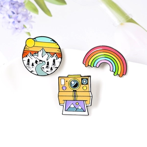 Set of enamel pins featuring a creative camera, rainbow, and mountain sunset design