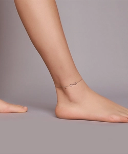 Detail of infinity and heart charms on a minimalist rose gold anklet worn on ankle